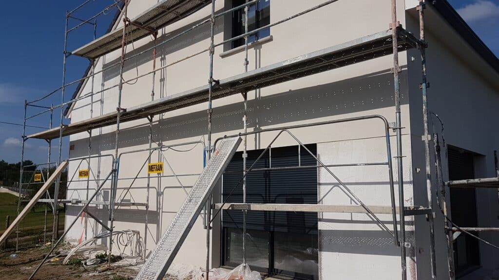 Maison en construction, façade claire fraîchement crépie, échafaudage MEFRAN et plateforme. Fenêtres, câbles au sol. Texte: 'CHARGE 300 daN/m²'.